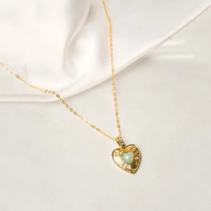 Stylish gold-tone necklace with a filled flat cable chain, an elegant heart pendant,with delicate filigree and a light opal blue stone in the center and a lobster claw clasp.