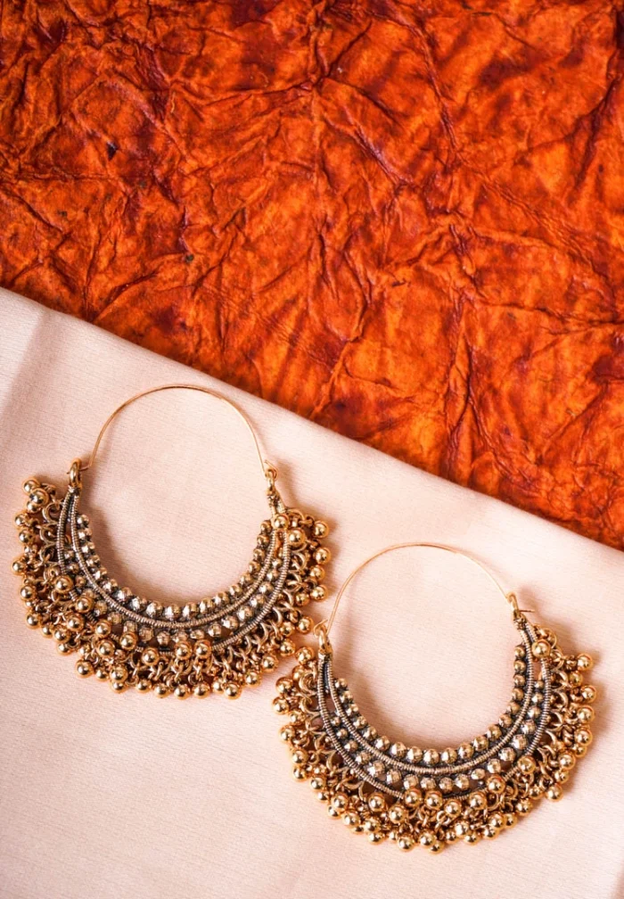 Ethnic metal drop earrings in an antique gold-tone finish, featuring a crescent design with fine bead detailing and dangling ghungroos, designed with a hinged back for secure wear.