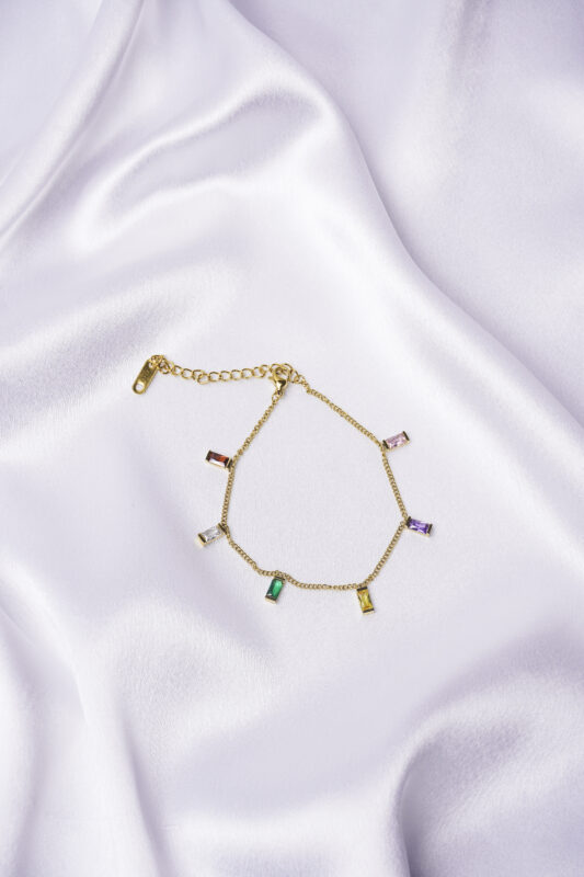Dainty curb chain bracelet in a gold-tone finish, accented with tiny dangling rectangular gemstones in various colors and a lobster claw clasp