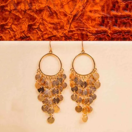 Rustic metal hoop earrings with an gold/silver finish, featuring gracefully dropping small, textured coin-like discs and a sleek curved hook closure
