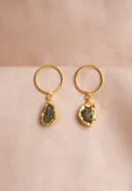 Handcrafted metal dangle earrings featuring a circular disc and a dangling raw teardrop gemstone in brownish-grey with golden and moss green undertones, secured with a push-back closure.