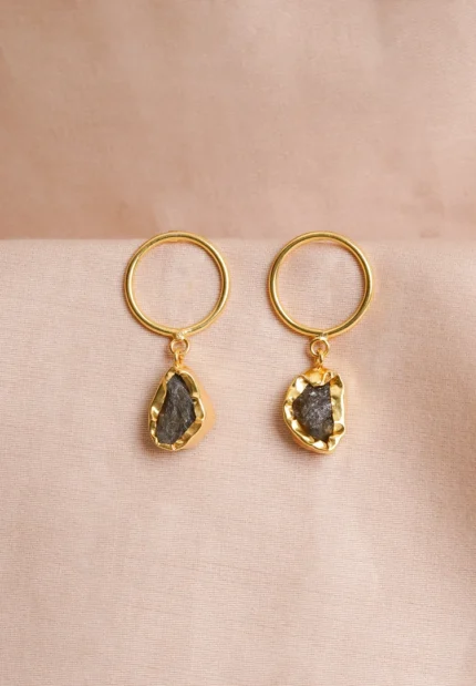 Handcrafted metal dangle earrings featuring a circular disc and a dangling raw teardrop gemstone in brownish-grey with golden and moss green undertones, secured with a push-back closure.