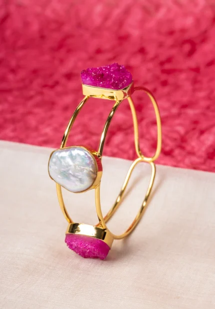 Chic organic-shaped cuff bracelet in a polished golden tone with black and pearl white accents, featuring asymmetrical black druzy stones on the sides and a central pearl-like detail.