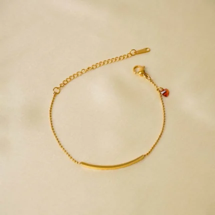 Minimalist gold-tone bracelet with a fine satellite chain, a sleek curved rectangular bar, and a petite orange heart charm, finished with a secure lobster claw clasp.