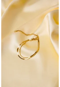 Elegant adjustable curb chain bracelet in a gold-tone finish, featuring a curved metallic wire centerpiece with a dangling spherical charm and a secure spring ring clasp.