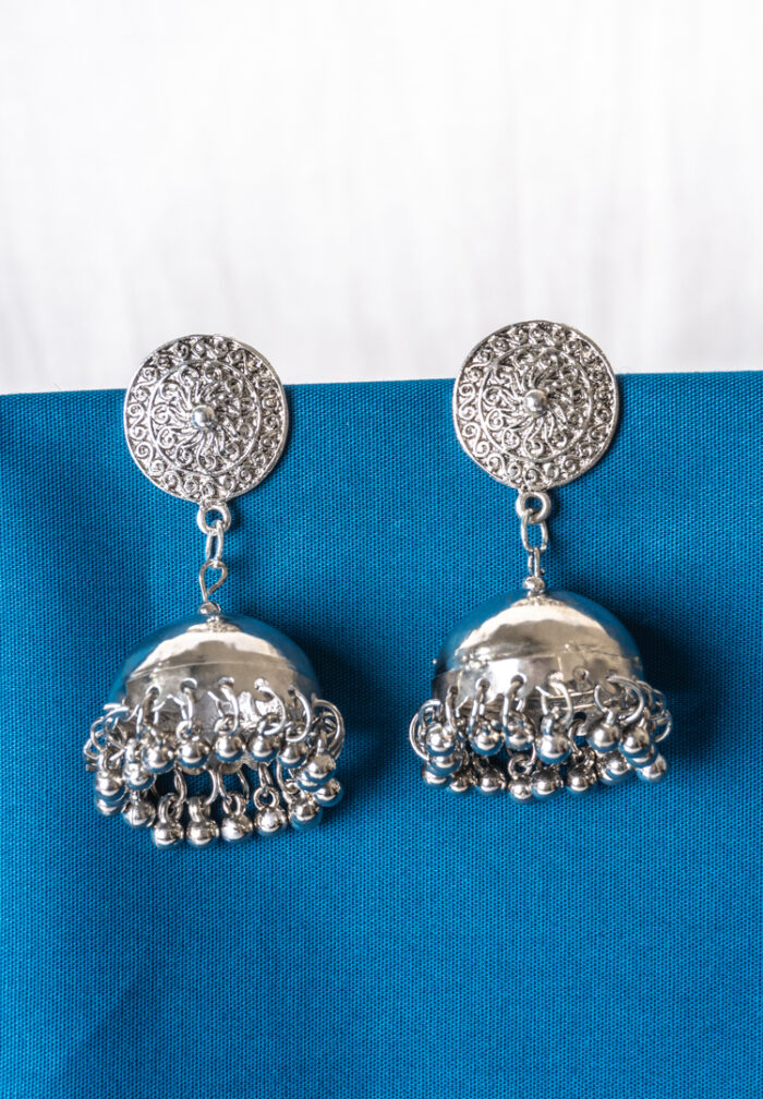 Oxidized silver-tone metal drop earring featuring a circular top with intricate floral detailing, attached to a jhumka adorned with ghungroos at the bottom, secured with a push-back closure.