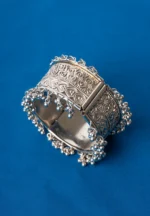 Oxidized silver-tone metal cuff bracelet featuring fine intricate detailing and adorned with ghungroos on both edges.