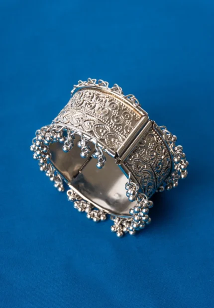 Oxidized silver-tone metal cuff bracelet featuring fine intricate detailing and adorned with ghungroos on both edges.