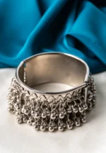 Oxidized silver-tone metal cuff bracelet featuring fine intricate detailing and adorned with ghungroos on both edges.