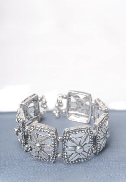 Handcrafted oxidized silver-tone metal cuff bracelet with evenly spaced floral square engravings, circular beadwork, and delicate ghungroo dangles.