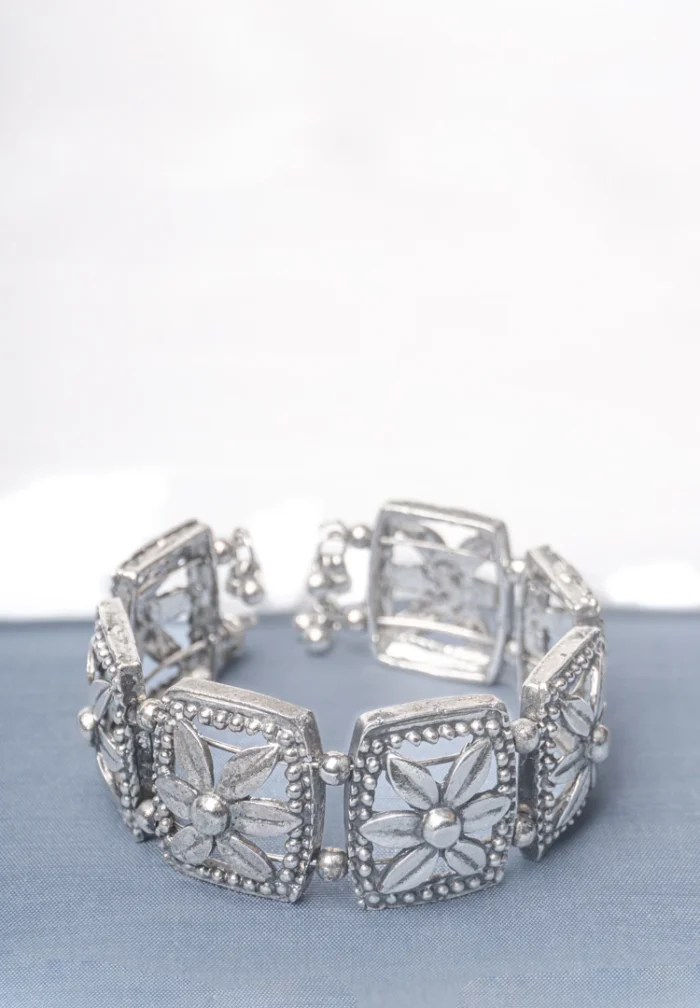 Handcrafted oxidized silver-tone metal cuff bracelet with evenly spaced floral square engravings, circular beadwork, and delicate ghungroo dangles.