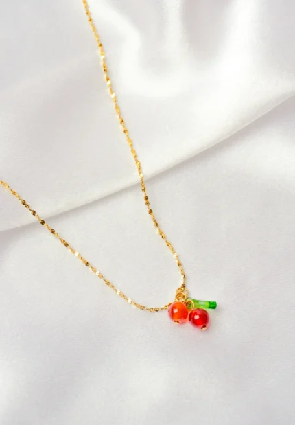 Playful and stylish gold-tone necklace with a textured chain, featuring a cute cherry pendant with two glossy cherries and a small green leaf, secured with a lobster claw closure