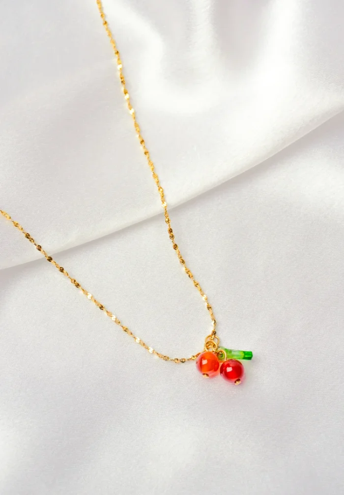 Playful and stylish gold-tone necklace with a textured chain, featuring a cute cherry pendant with two glossy cherries and a small green leaf, secured with a lobster claw closure