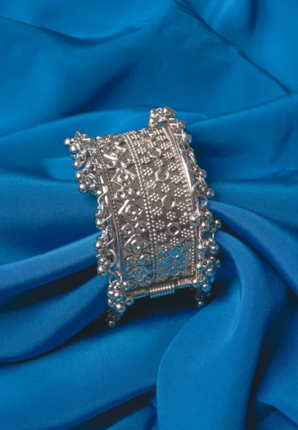 Oxidized silver-tone metal cuff bracelet featuring fine intricate detailing and adorned with ghungroos on both edges.