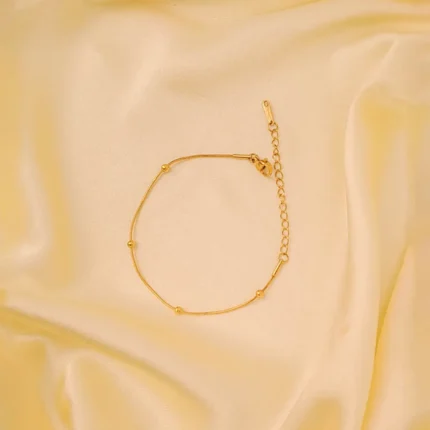 Polished gold-tone snake chain bracelet featuring evenly spaced small circular beads and a secure lobster claw clasp