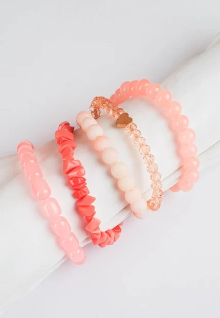 Pack of five pink and coral beaded stretch bracelets, one with a heart charm and one with a gold chain