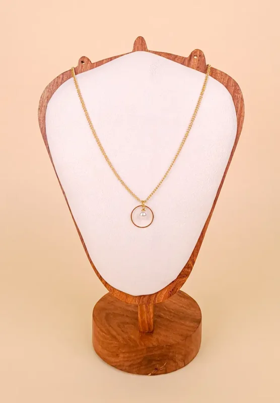 A delicate, gold-toned chain necklace featuring a single round pendant: a faux pearl suspended in the center of a thin, open, circular gold frame.