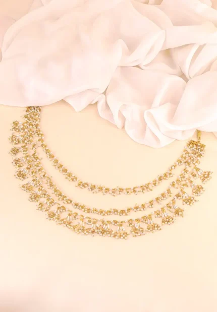 Three-tiered gold-tone necklace (Haar) featuring linked floral motifs with delicate white pearl beads cascading from the lower edge.