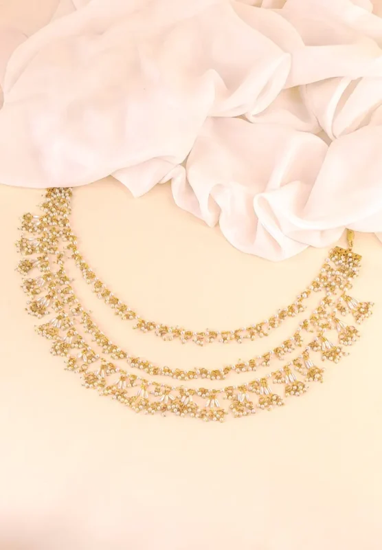 Three-tiered gold-tone necklace (Haar) featuring linked floral motifs with delicate white pearl beads cascading from the lower edge.