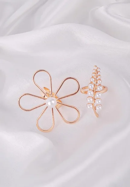 "Two gold-toned cocktail rings with faux pearls: a five-petal magnolia wire ring and a textured vine-inspired pearl band. Elegant, nature-inspired designs perfect for stacking or wearing individually."