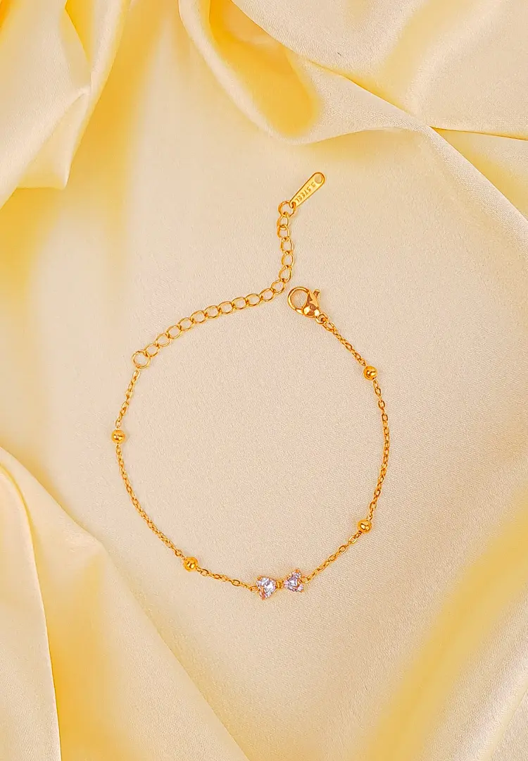 TH-598 (1) Gold-toned bracelet with a thin beaded chain and a small, white gemstone bow charm in the center.