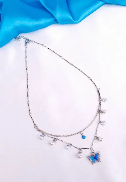 Double-layered silver necklace featuring a blue butterfly charm, adorned with pearl and crystal accents.