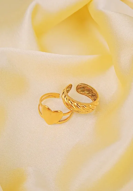A pair of adjustable gold-toned rings: one is a thick braided or croissant style, and the other is a thin stack ring with a heart shape.