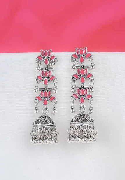 Long tiered Jhumka earring featuring an oxidized silver finish. It has three linked floral sections with dark pink enamel accents, leading down to a decorative bell-shaped drop with dangling beads.