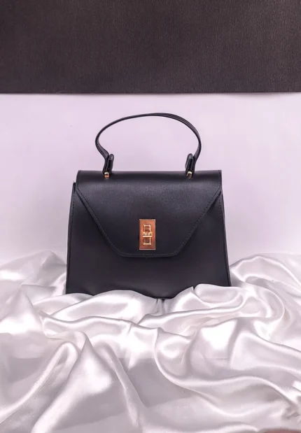 Black sling bag with structured flap design and gold twist-lock closure, featuring an adjustable strap — chic everyday bag