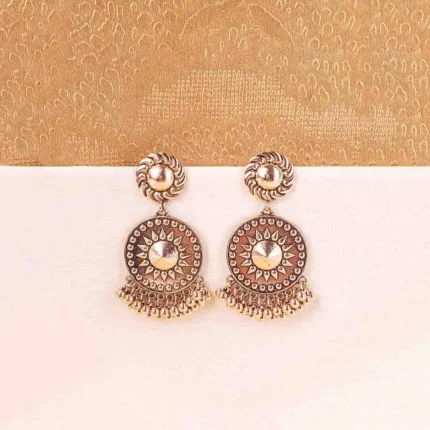 Large, antique matte gold-tone drop earring featuring a circular disc with a raised sunburst or Chakra motif in the center, hanging from a swirling stud. The bottom is fringed with small, round ghungroo beads.