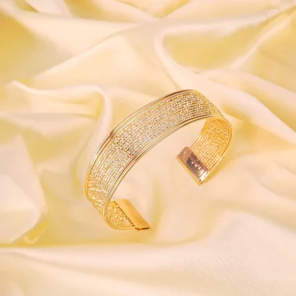 a broad, open-ended gold-colored cuff bracelet with a finely textured, almost woven appearance