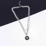 A silver-toned layered necklace is displayed on a dark gray laptop keyboard. The necklace features two main strands: one is a chunky curb chain with a circular pendant depicting a silver teddy bear, and the other is a finer chain adorned with five evenly spaced, lustrous white pearls. Both chains connect at the clasp end.