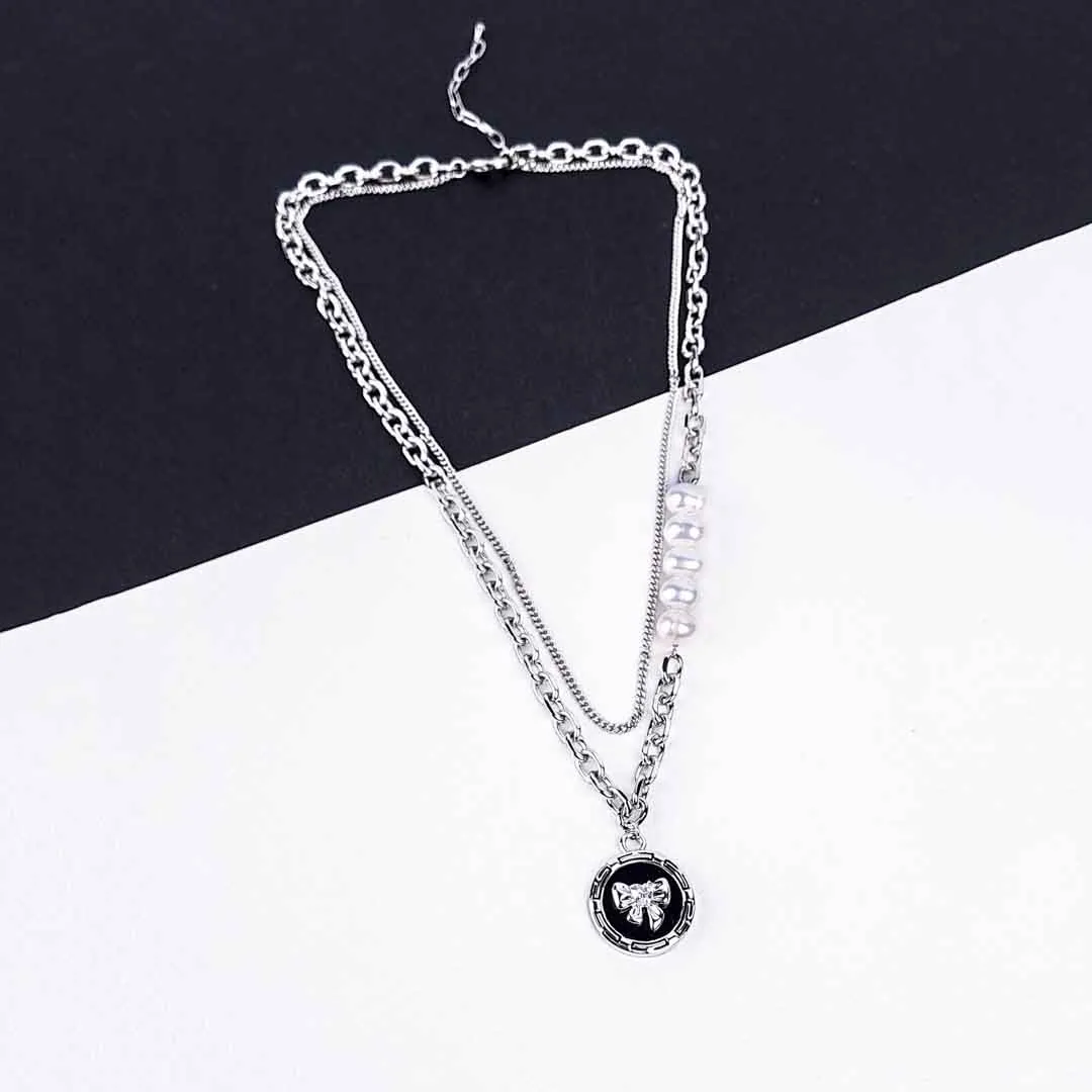 20251120_122422 A silver-toned layered necklace is displayed on a dark gray laptop keyboard. The necklace features two main strands: one is a chunky curb chain with a circular pendant depicting a silver teddy bear, and the other is a finer chain adorned with five evenly spaced, lustrous white pearls. Both chains connect at the clasp end.