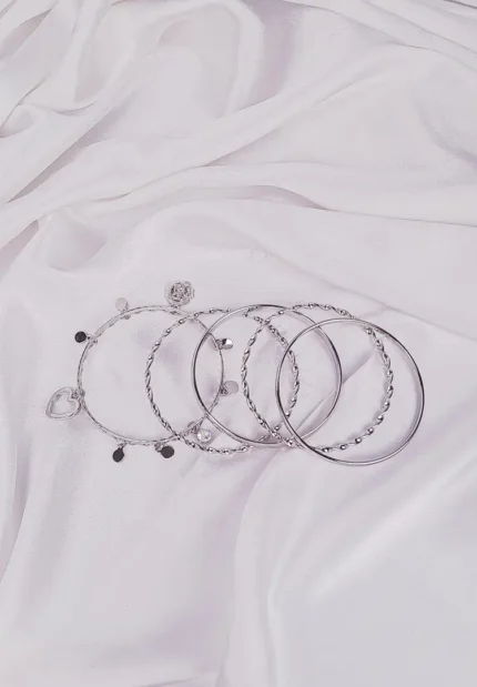 Set of six silver bangles with polished, twisted, and beaded designs, including a heart charm detail, crafted in lightweight slip-on style for versatile wear.