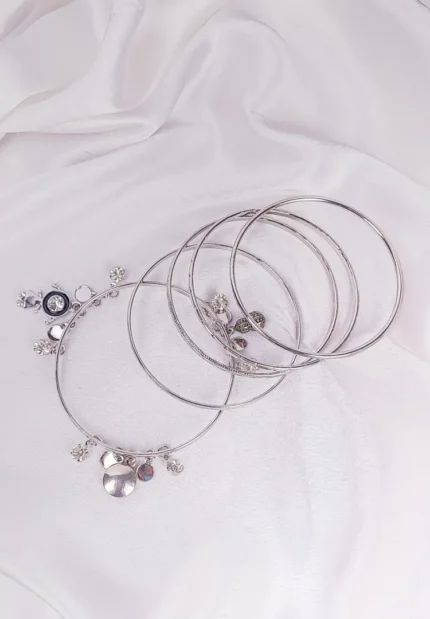 Set of five polished silver bangles, one styled with hanging charms and sleek finish, ideal for trendy stacked look.