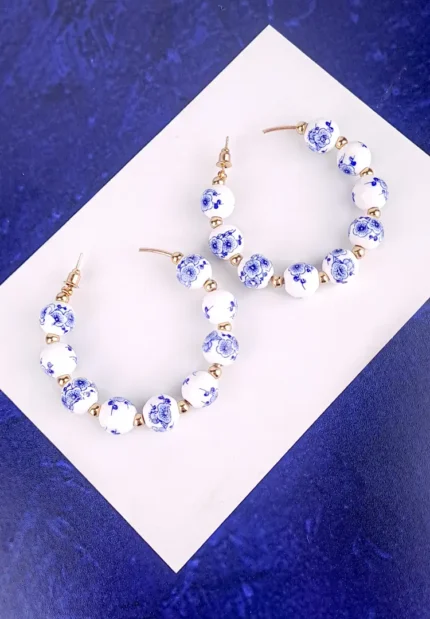 White bead hoop earrings with blue floral beads gold accents and push-back closure.