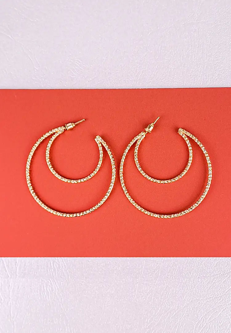 th - 2025-12-02T164828.017 Gold layered hoop earrings with textured polished finish and push‑back closure, featuring three interlaced arcs for a sculptural look.
