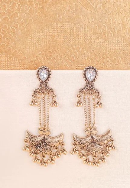 Ornate antique gold drop earring featuring a teardrop-shaped clear stone stud connected by delicate chains to a heavy, decorative crescent-shaped pendant adorned with small dangling metallic ghungroo beads.