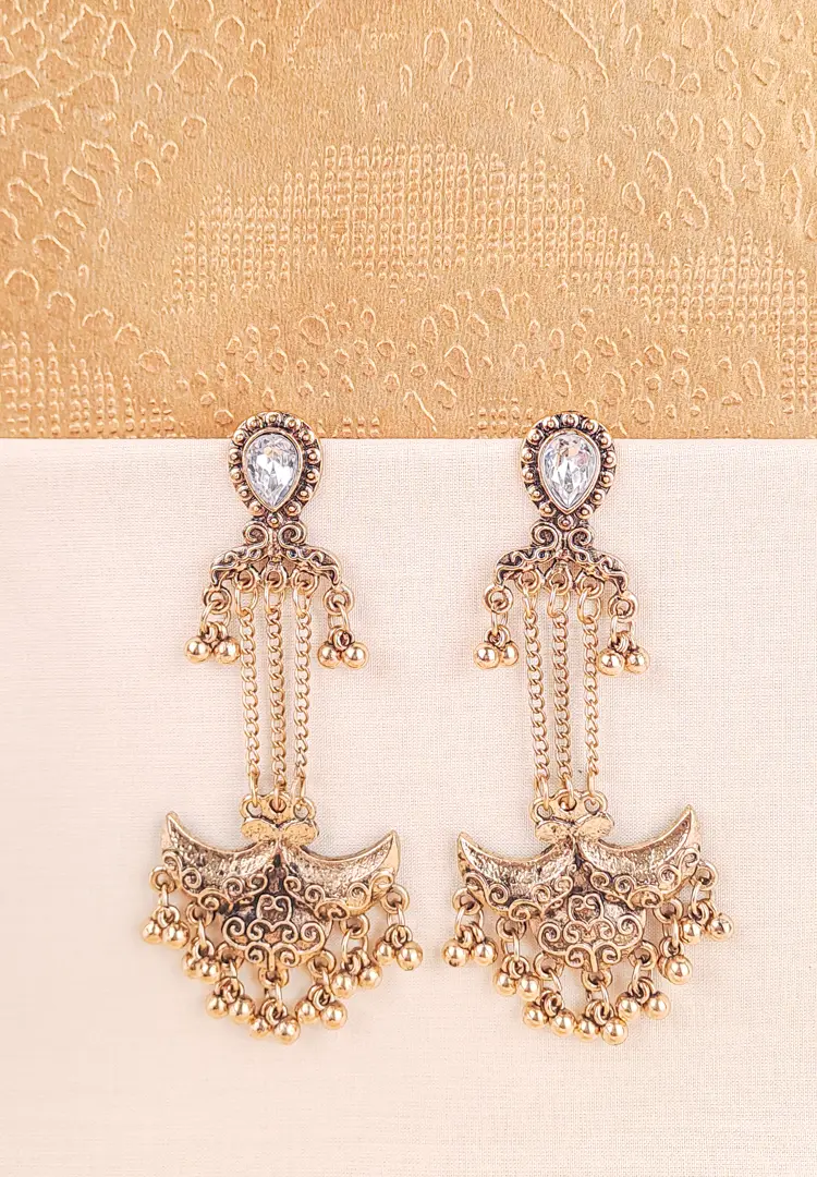 th - 2025-12-02T181700.644 Ornate antique gold drop earring featuring a teardrop-shaped clear stone stud connected by delicate chains to a heavy, decorative crescent-shaped pendant adorned with small dangling metallic ghungroo beads.