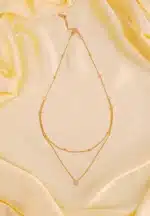 Gold layered necklace with bead accents, crystal charm, and adjustable lobster clasp.