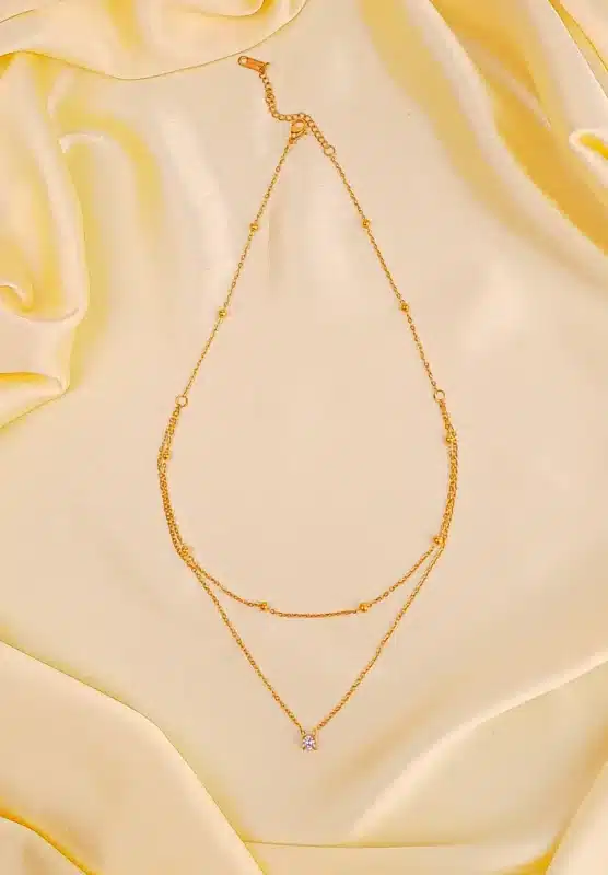 Gold layered necklace with bead accents, crystal charm, and adjustable lobster clasp.