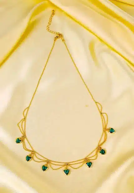 Layered gold necklace with emerald green heart charms and lobster clasp.