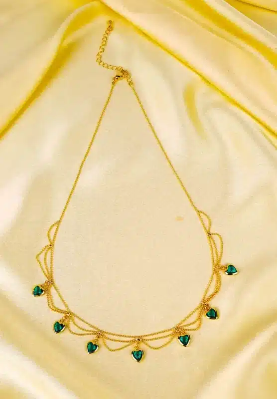 Layered gold necklace with emerald green heart charms and lobster clasp.