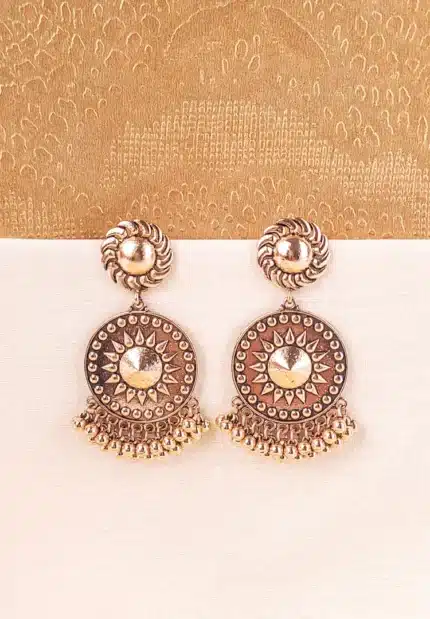 Large, antique matte gold-tone drop earring featuring a circular disc with a raised sunburst or Chakra motif in the center, hanging from a swirling stud. The bottom is fringed with small, round ghungroo beads.
