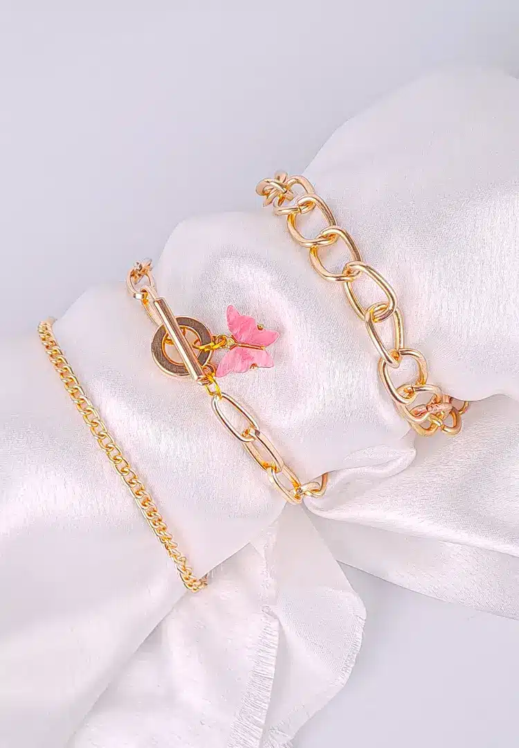 th - 2025-12-12T154130.943 Three gold chain bracelets, one with large links, one classic, one with a pink butterfly charm and adjustable closures.