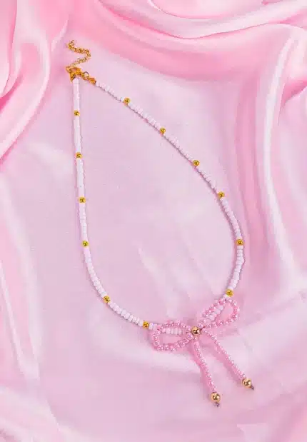 White and gold beaded necklace with a pink pearl bow pendant and gold adjustable clasp, styled for a modern, feminine look.