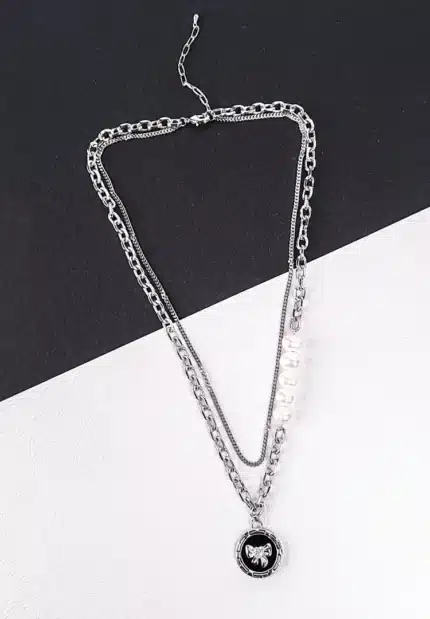 A silver-toned layered necklace is displayed on a dark gray laptop keyboard. The necklace features two main strands: one is a chunky curb chain with a circular pendant depicting a silver teddy bear, and the other is a finer chain adorned with five evenly spaced, lustrous white pearls. Both chains connect at the clasp end.