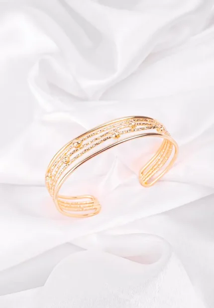 a gold-colored bangle bracelet composed of multiple textured bands, including beaded and dotted designs
