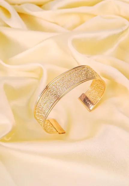 a broad, open-ended gold-colored cuff bracelet with a finely textured, almost woven appearance