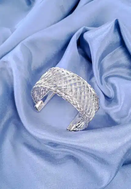 The bracelet features a dense, intricate, and evenly woven mesh pattern made from numerous thin, shiny gold wires, giving it a rich texture. The cuff is open at the bottom.